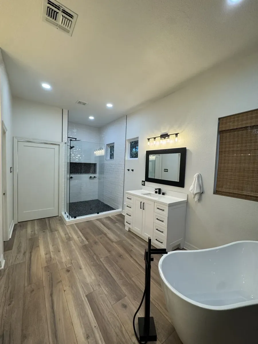 Full bathroom remodel overview showing LVP floors, glass shower, vanity and freestanding tub in San Antonio, TX