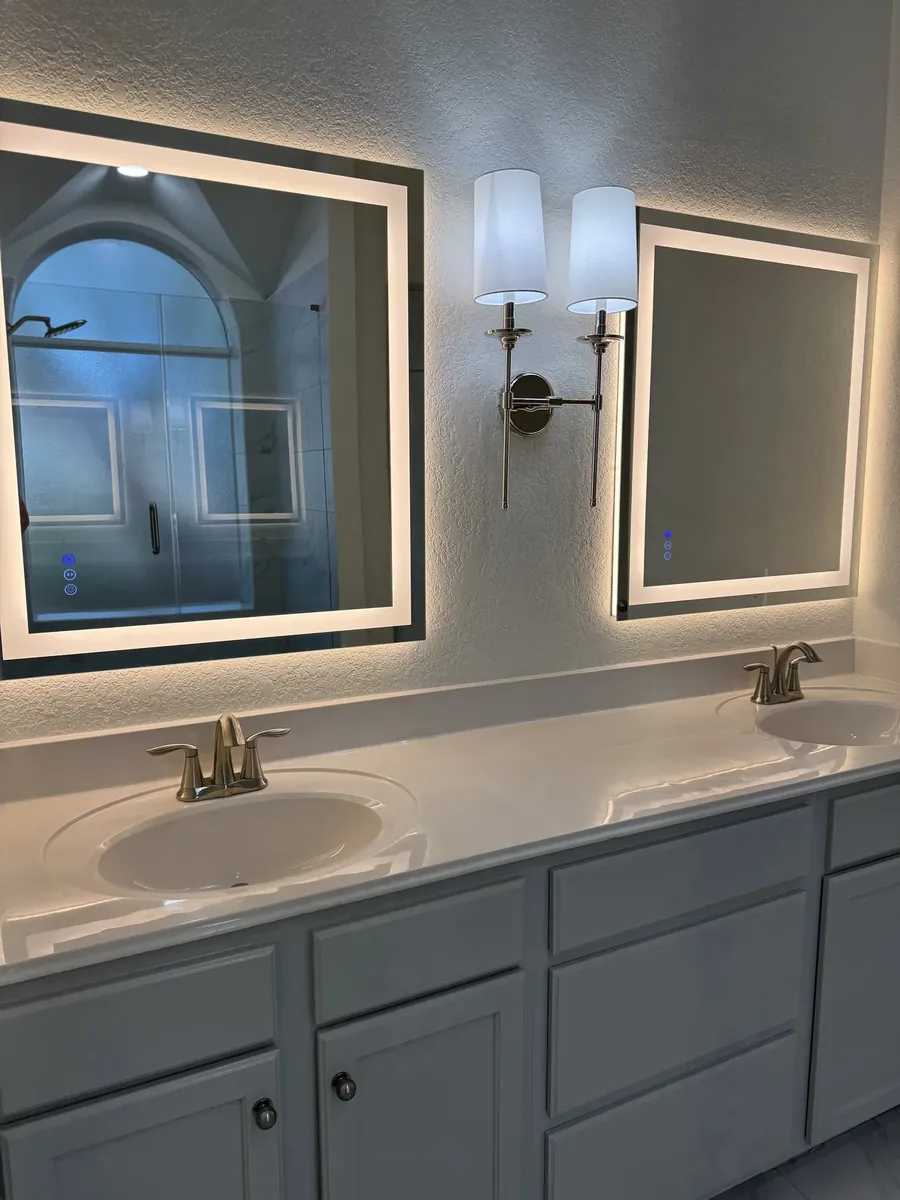 Double vanity with dual LED backlit mirrors and wall sconce in remodeled bathroom, San Antonio, TX